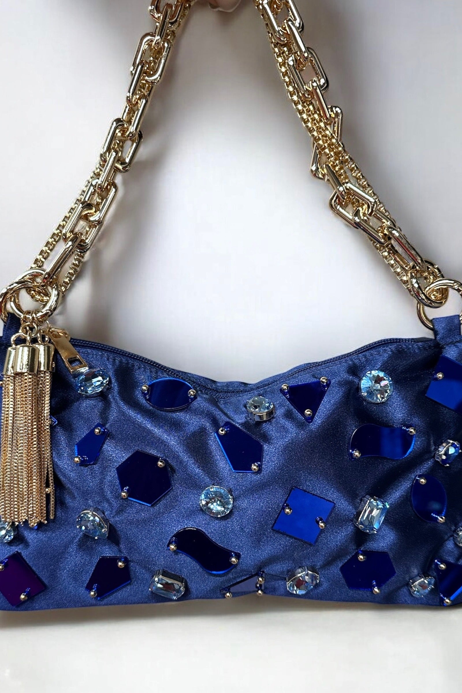 Blue handbag with gemstones and a gold chain strap on a white background